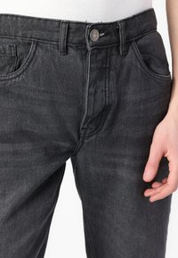 Jeans in denim nero con un classico design a cinque tasche, chiusura frontale con bottone e una sottile texture con una finitura leggermente sbiadita.