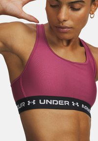 Sportbeha in ros�é kleur, met een zwarte elastische band met de tekst "UNDER ARMOUR". Gladde stof met een aansluitend ontwerp en verstelbare banden.