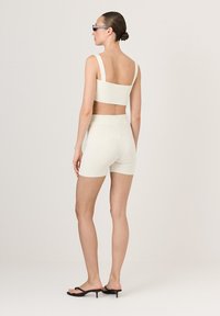 Dopasowany zestaw z krótkim topem i szortami z prążkowanej dzianiny w jasnym kremowym kolorze, z szerokimi ramiączkami i wysokim stanem, uzupełniony czarnymi sandałami na wysokim obcasie.