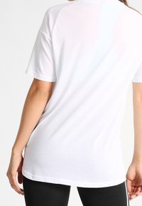 Bílé tričko s krátkými rukávy, volným střihem a zaobleným lemem. Měkká, hladká bavlněná látka s raglánovými rukávy pro pohodlí.