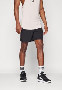 Μαύρες αθλητικές βερμούδες με ίσια γραμμή, φορεμένες με ανοιχτό ροζ αμάνικο μπλουζάκι, μαύρα αθλητικά παπούτσια και λευκές κάλτσες με μαύρες ρίγες.