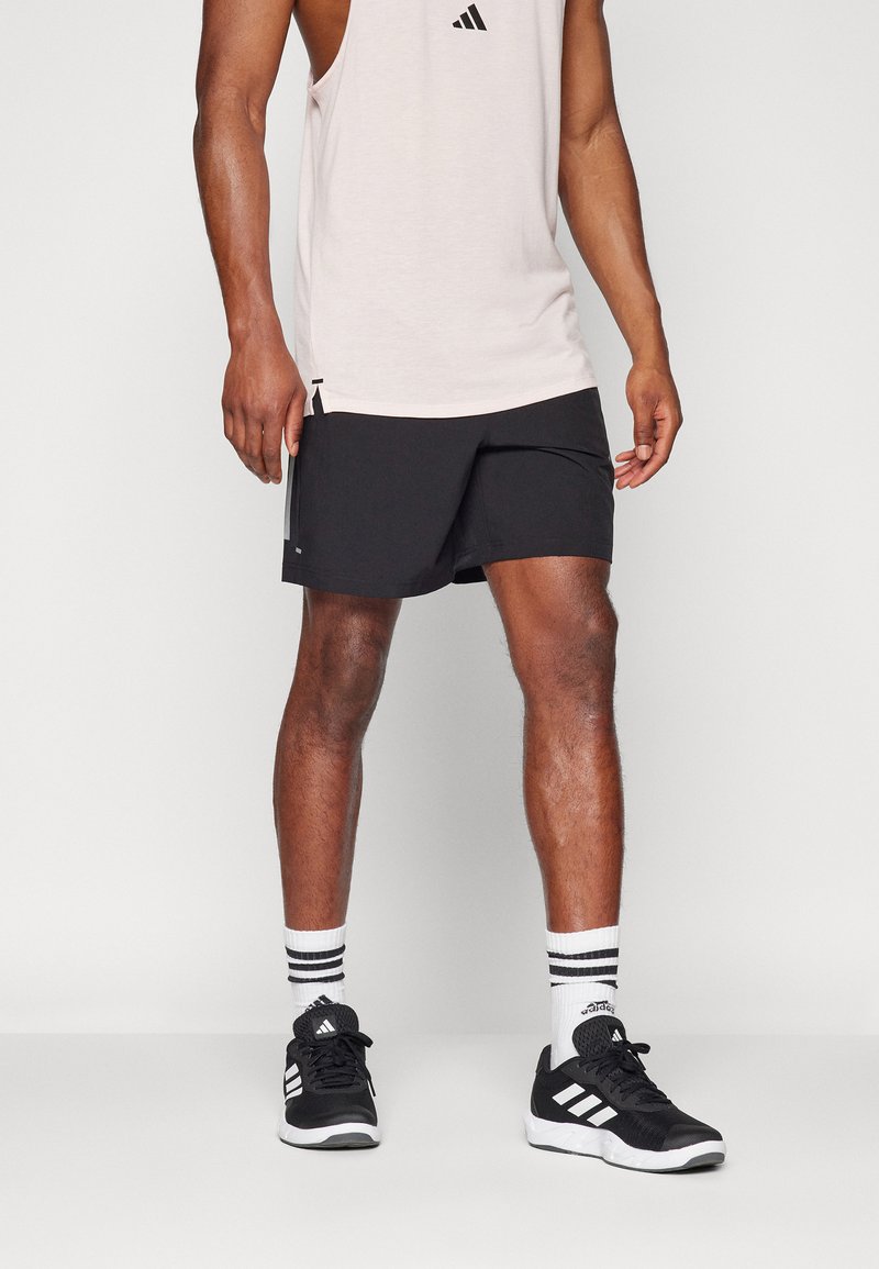 Μαύρες αθλητικές βερμούδες με ίσια γραμμή, φορεμένες με ανοιχτό ροζ αμάνικο μπλουζάκι, μαύρα αθλητικά παπούτσια και λευκές κάλτσες με μαύρες ρίγες.