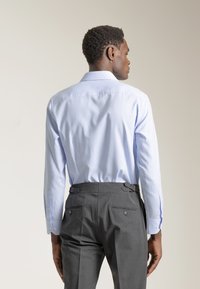 Camisa de vestir azul claro con mangas largas, tejido texturizado, puños abotonados, combinada con pantalones grises con ajustadores laterales y bolsillos traseros.