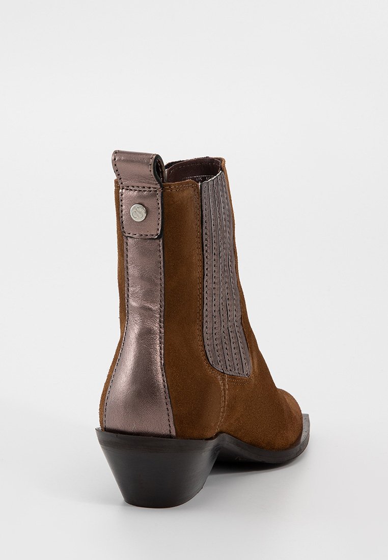 Bruine suède enkelboot met een metallic bronzen paneel, geribbelde textuur, een ronde neus en een kleine hak. Bevat een trekband en een metalen accent.