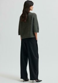 Hrnčiarový tmavozelený pletený sveter s trojštvrťovými rukávmi, skombinovaný s voľnými čiernymi nohavicami s vysokým pásom. Viditeľné detaily textúrovanej látky.