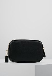 Musta nahkainen kosmetiikkapussi, jossa on teksturoitu pinta, suorakulmainen muoto, kultainen vetoketju ja pieni bränditagi sivussa.