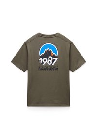 Olivově zelené tričko s krátkým rukávem, které zobrazuje horskou grafiku, text "1987" a "Napapijri geographic" v černé a modré. Hladká textura látky.