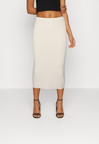 Stickad, ljusgrå midikjol med ribbad textur och figurnära siluett, i kombination med svarta remsandaler med hög klack.