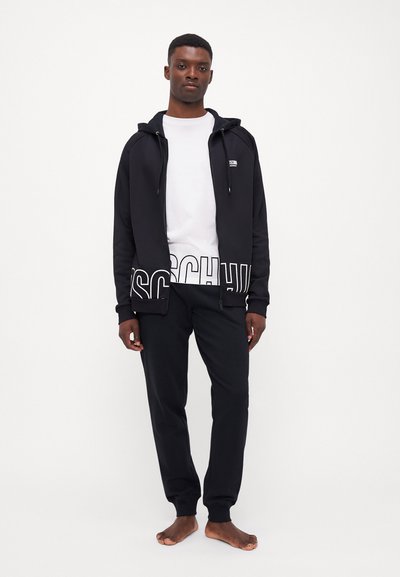 Black zip-up hoodie with front pockets and white logo, layered over a white T-shirt, paired with black jogger pants.