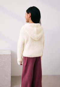 Hoodie tricoté en fil duveteux de couleur crème avec un motif texturé, associé à un pantalon ample bordeaux. Présente un col bas et décontracté ainsi que des poignets ajustés.