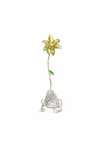 Flor de vidrio amarillo con cinco pétalos y una hoja verde, montada sobre una base de cristal transparente facetado, sostenida por un marco de metal dorado.