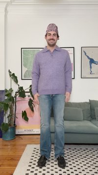 Suéter de punto lavanda con cuello, jeans azul claros y zapatos negros. Un gorro morado con estampado completa el conjunto. Ambiente interior.