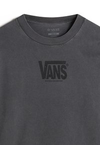 Dunkelgraues, lässig geschnittenes T-Shirt mit rundem Ausschnitt. Auf der Vorderseite befindet sich ein schwarzes Vans-Logo und der Text "SACRED GEOMETRY".