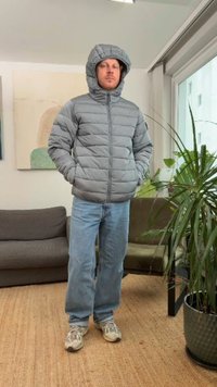 Šedá prešívaná bunda s kapucňou, s prešívaným vzorom. Nosená na svetlomodrých džínsach a teniskách. Vnútorné prostredie s zeleňou.