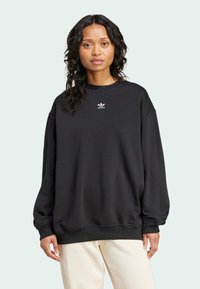 Svart sweatshirt med rund halsringning och långa, lätt puffade ärmar. Har en liten vit Adidas-logotyp på bröstet. Mjukt tyg.