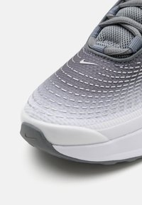 Nike futócipő, amelynek szürke színátmenetes felsőrésze, texturált hálós anyaga, fehér talpa van, és a lábujjaknál jellegzetes fehér swoosh logó található.