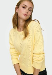Pull jaune en tricot avec col rond, orné de motifs de cœurs et de poignets côtelés. La texture est douce et légère.