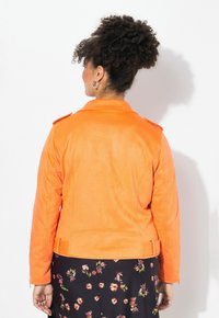 Veste en simili cuir orange avec un col structuré, des épaulettes et des coutures détaillées. Texture lisse, design ajusté.
