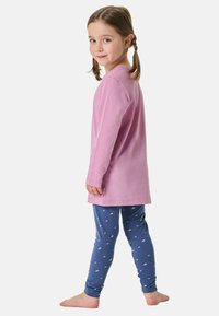 Rosa Langarmshirt kombiniert mit blauen Leggings mit weißen Mustern. Das Outfit besteht aus weichem Stoff und ist geeignet für lässige Kleidung.