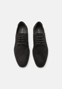 Chaussures oxford en suède noir avec une texture lisse, un bout arrondi et un système de laçage. Présente un design minimaliste avec un branding subtil à l'intérieur.