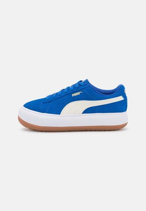Niebieski sneaker Puma z białym paskiem po boku, gumową podeszwą i sznurowanym zapięciem na jednolitym jasnym tle.