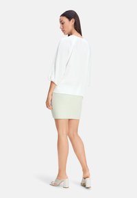 Weißes, lässig geschnittenes Oberteil mit Puffärmeln, kombiniert mit einem strukturierten, hellgrünen Minirock und offenen Blockabsatzsandalen.