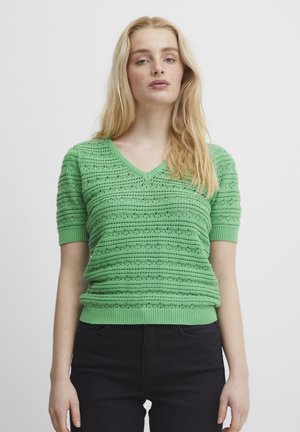 Suéter verde de punto con escote en V, mangas cortas, rayas texturizadas y bajo acanalado. Combinado con pantalones negros.