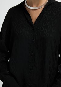 Black button-up shirt with a subtle leopard print pattern, long sleeves, and a collar. The fabric has a smooth, soft texture.