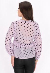 Lavendel gennemsigtig bluse med sorte prikker, flæser ved skuldrene og indsnævret talje. Lange ærmer med puffet design og rund halsudskæring.