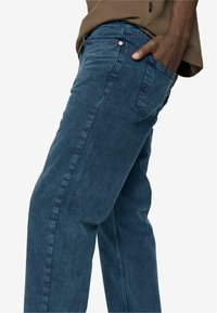 Modri jeans s sproščenim krojem, ki imajo pet žepov in vidno šivano strukturo vzdolž šivov. Tekstura je videti mehka.