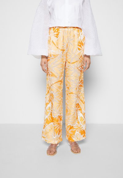 Calças largas com padrão floral amarelo e detalhes brancos. Leves, de corte solto, combinadas com uma blusa branca texturizada e sandálias transparentes.