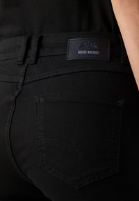 Zwarte denim jeans met een subtiele gestructureerde stof, een logo patch op de tailleband en een enkele achterzak met decoratieve stiksels.