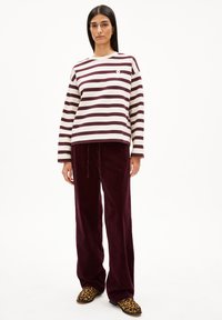 Gestreepte lange mouwen shirt in bordeauxrood en crème, gecombineerd met bordeauxrode corduroy broek. Dierlijke print instappers maken de outfit compleet.