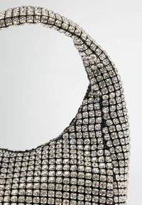 Ehtetud rhinestone'idega must käekott, millel on allaeenduv käepide, näidates tekstuurset pinda ja väikseid läikivaid kristalle üle kogu pinna.