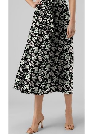 Schwarzes Midikleid mit floralen Mustern in Weiß und Grün, fließendem Stoff und einem gebundenen Taillenakzent. Kombiniert mit nackten Riemchenschuhen.