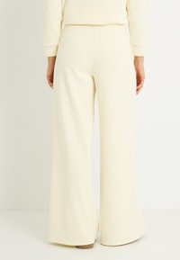 Pantalones de pierna ancha color crema, hechos de material de punto acanalado, con cintura alta y textura suave, con un brillo sutil.