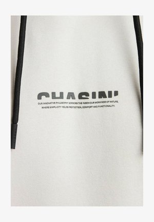 Baltas audinys su kapuce, kuris turi juodą virvutę. Juodu spausdintu tekstu užrašyta "CHASIN'" su filosofiniu teiginiu žemiau.