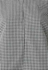 Svart och vit rutigt tyg med litet gingham-mönster, som har en slät textur och vertikal sömdetalj i mitten.