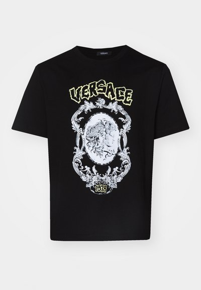 Must musta T-särk, millel on detailne valge graafiline disain keskel oleva medaliiniga, mille ülal on tekst "VERSACE" ja all "1978".