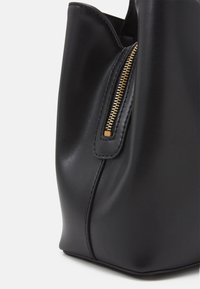 Černá kožená taška tote s hladkou texturou, vybavená zlatým zipem a pevnou strukturou. Viditelná je i další boční kapsa na zip.