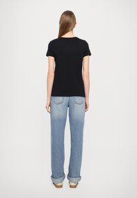 Svart t-skjorte med korte ermer og rund hals, sammen med lyseblå rettskårne jeans, oppbrettet ved anklene, og sko med tresåler.