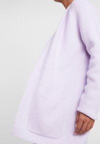 Jasnofioletowy sweter z dzianiny o luźnym kroju, z głębokim dekoltem i kieszenią z przodu. Teksturowany materiał z długimi rękawami i bez zapięć.