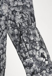 Černobílá vzorovaná bunda s designem lesa, texturovaná tkanina, viditelný detail zipu a trhlinka na tkanině.