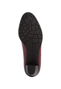 Suola in gomma di una scarpa con una superficie testurizzata e decorata. La parte superiore è color mogano con una forma elegante e un piccolo accentuato tacco.
