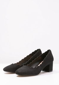 Black suede high-heeled shoes with scalloped edges, rounded toe, and a chunky block heel, featuring a smooth texture.
