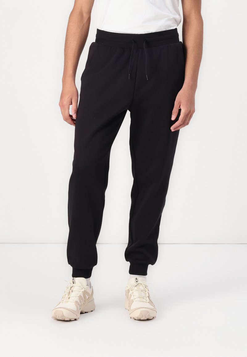Sorte bomulds joggers med elastisk talje og håndled, der har en afslappet pasform og sidelommer. Matchende med beige sneakers.