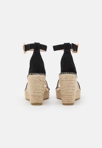 Black suede wedge sandals with an espadrille rope platform, buckle ankle strap, and open back design. Textured surface, approximately 3-4 inches high.