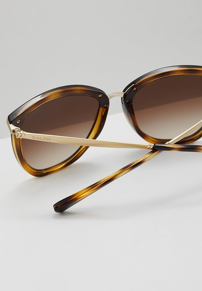 Tortoise shell stiliaus saulės akiniai su gradientiniais rudos spalvos lęšiais, auksinės spalvos metaliniais akcentais ir katės akies formos detalėmis ant rėmelių ir šventyklų.
