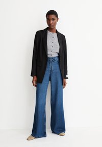 Blazer noir, chemise à boutons grise et jeans en denim bleu à jambes larges. Tissu lisse, design ajusté et coupe décontractée avec taille élastique.