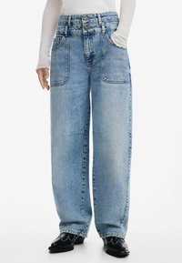 Jean large bleu clair en denim, présentant une taille haute avec fermeture à double bouton, des poches avant et un dégradé subtil.